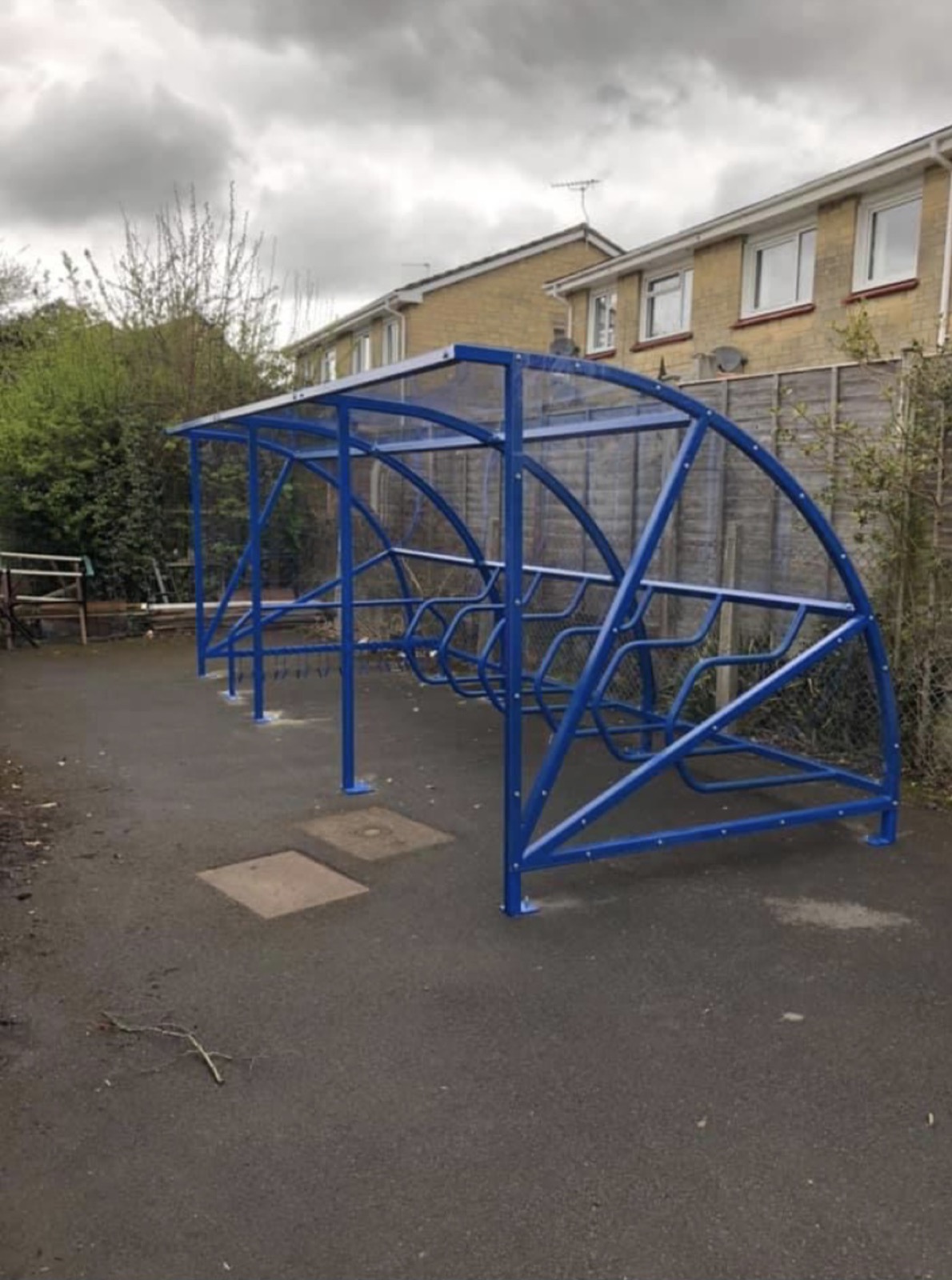 Blue cantilever cycle shelter by a hedge
