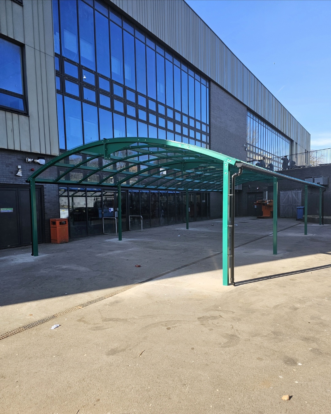 Angled view of the free-standing green arched dining canopy in front of the glazed building frontage