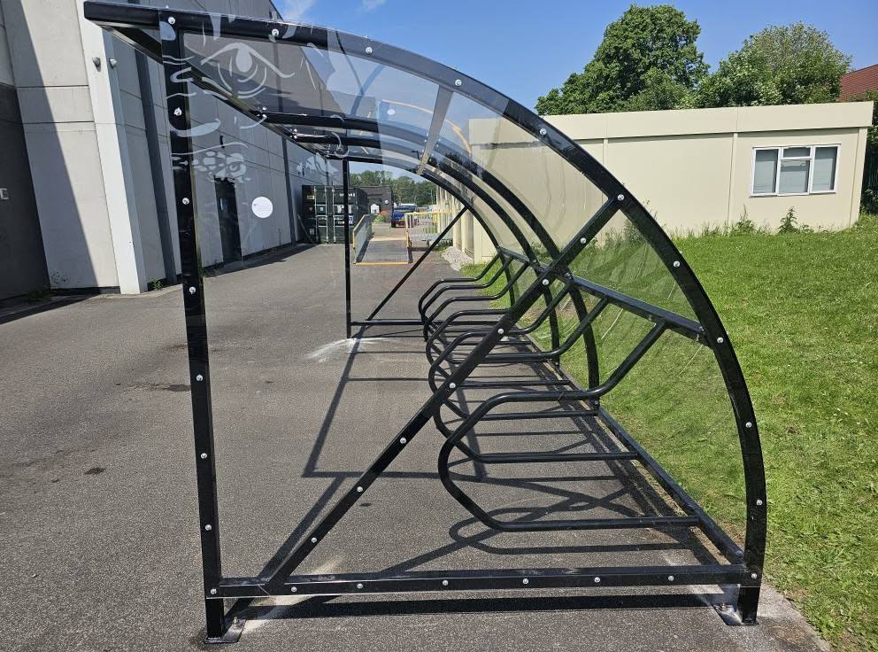 Interior view along the cycle rack beneath the shelter's curved roof and bolted frame
