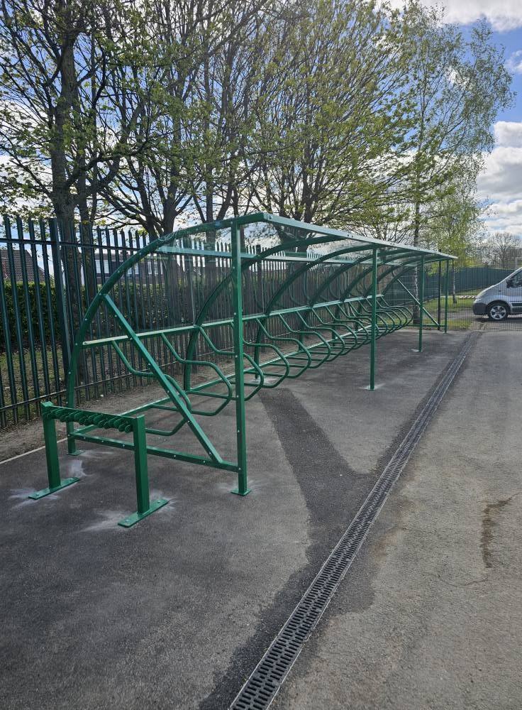 Green curved cycle shelter with internal bike rails and a separate scooter rack at Fens Primary School, Hartlepool
