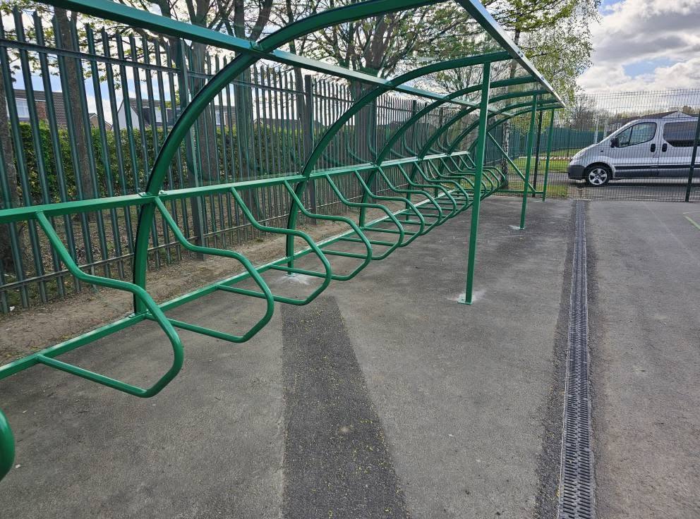 Close view inside the green cycle shelter showing the curved frame and rows of bike rails