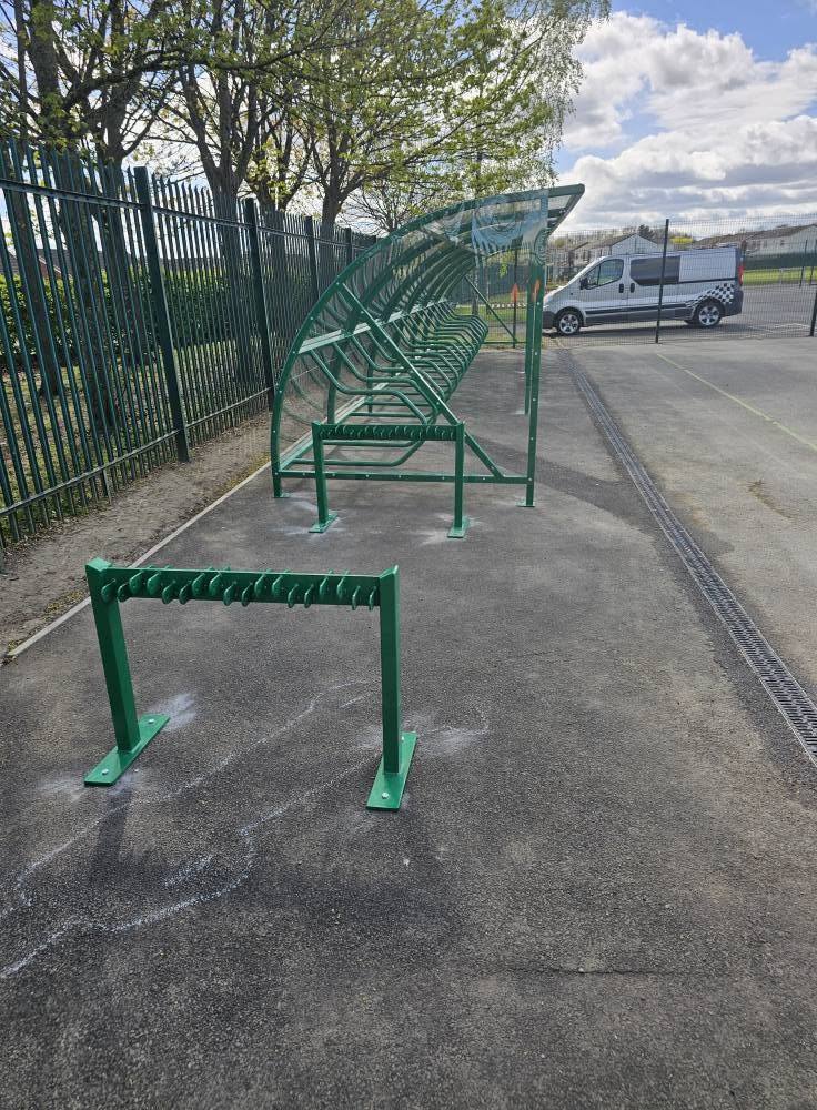 End-on view of the green cycle shelter with a scooter rack in the foreground on tarmac