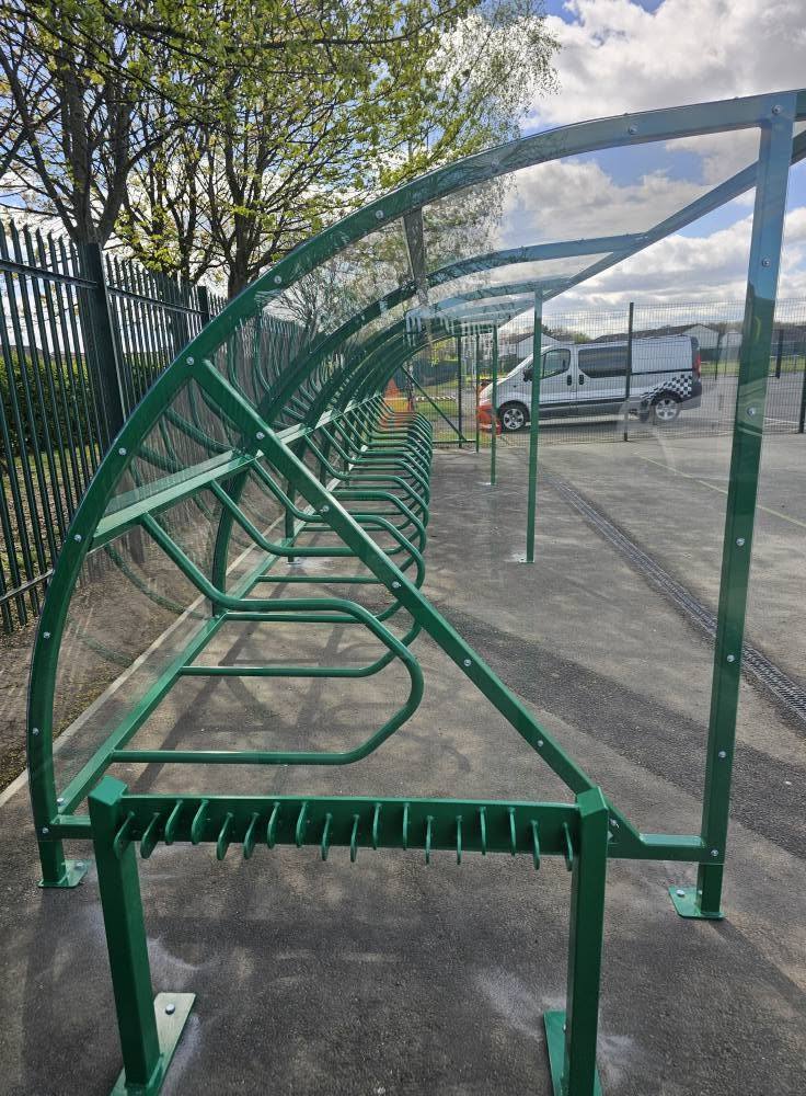 Interior length of the green cycle shelter showing bike rails under the clear curved roof
