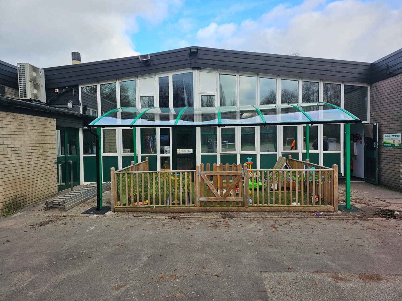 Green curved canopy over a fenced early-years play area outside a school