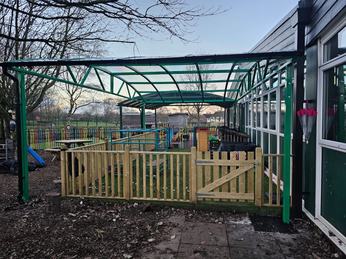 Angled view of a green curved canopy framing a fenced school play space
