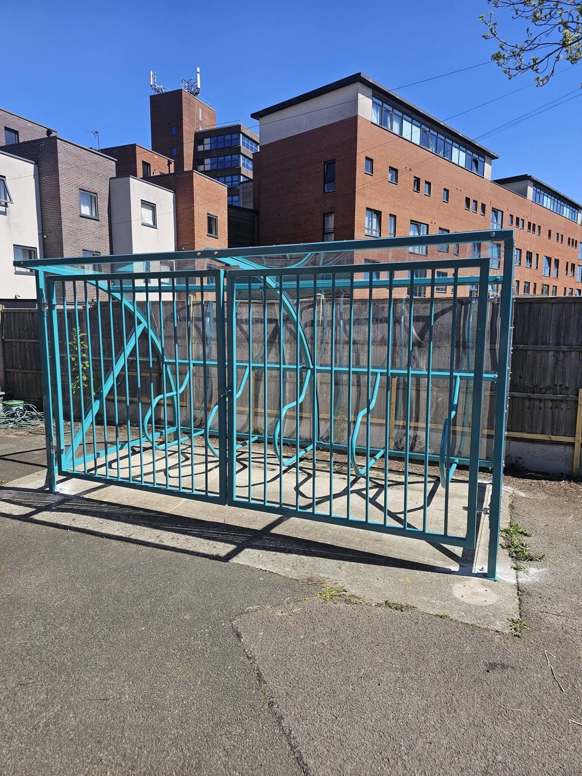 Teal cycle shelter with locked barred security gates in front of flats at Hideaway Youth Project, Manchester