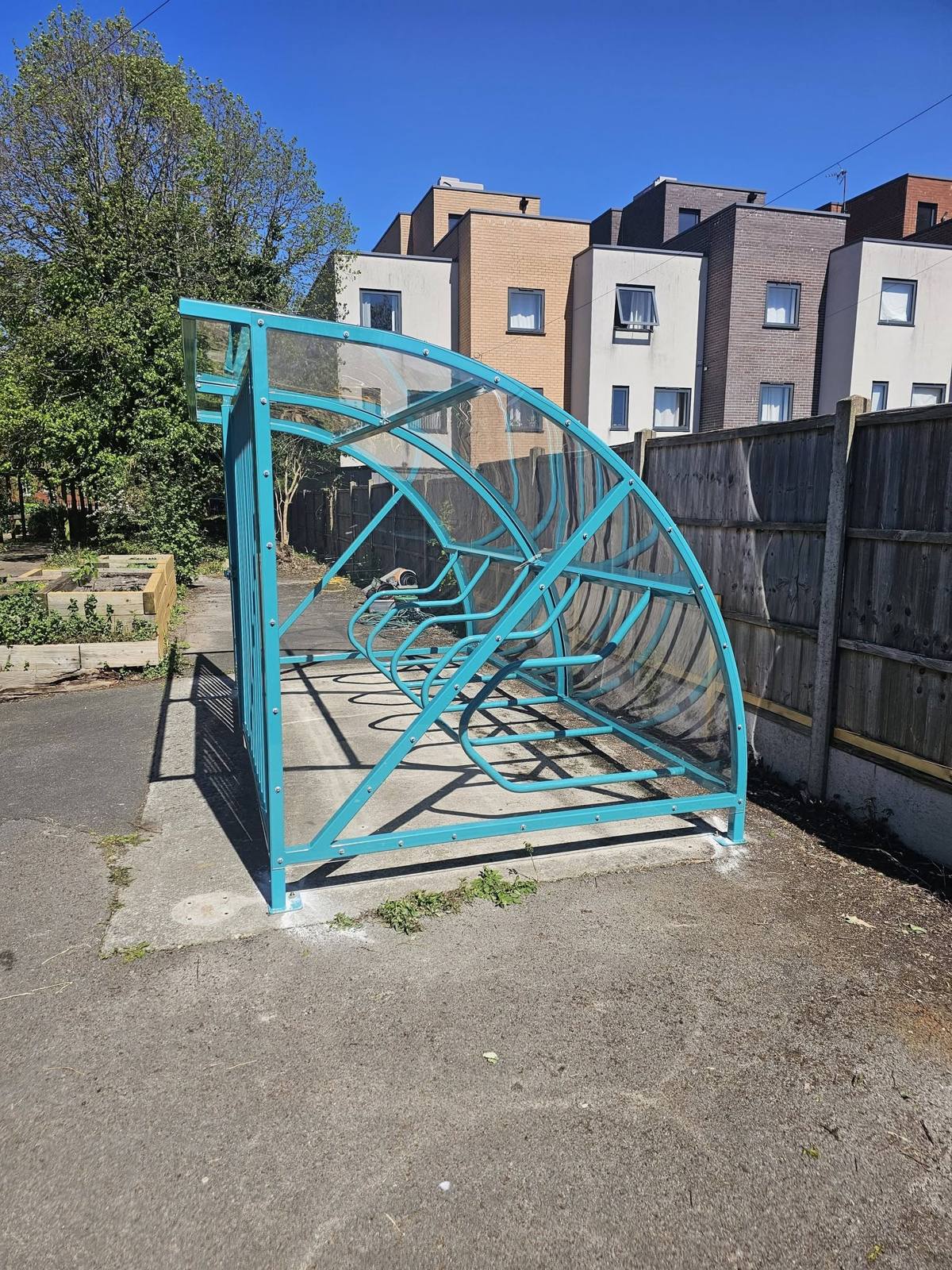 Side view of the curved cycle shelter with cycle racks beside a garden and timber fence