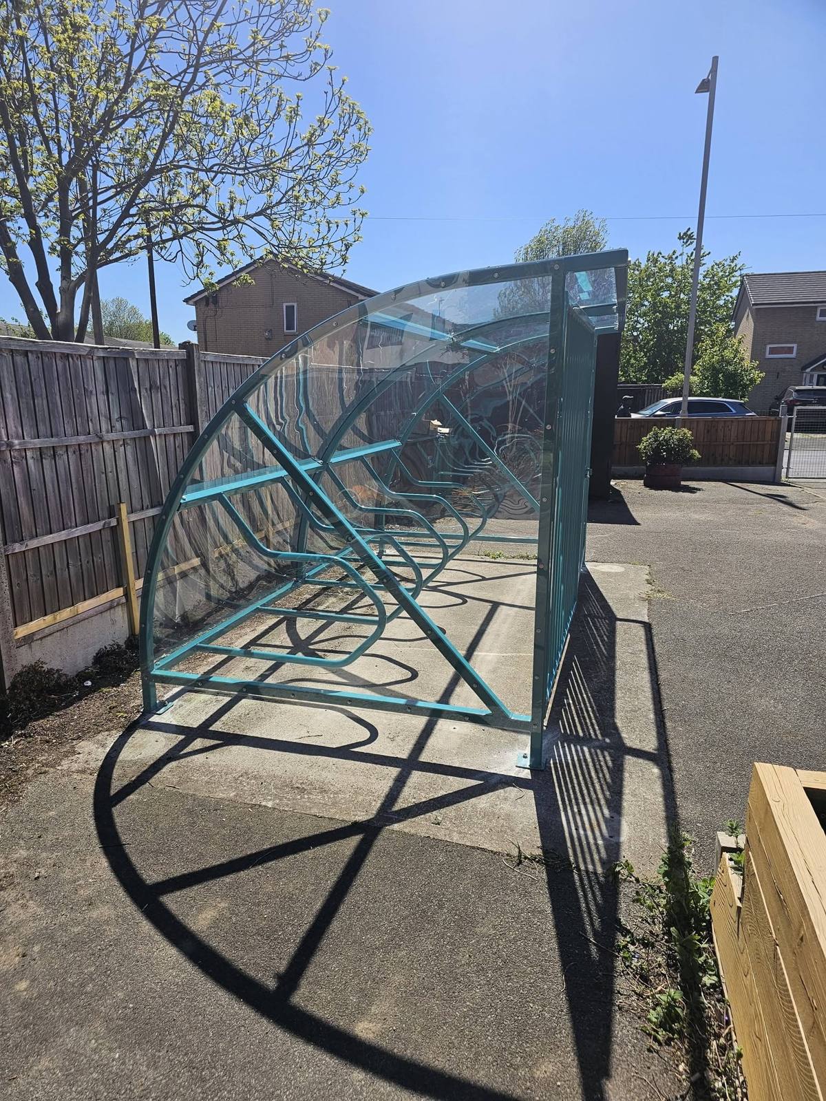 Low-angle side view of the clear-roofed cycle shelter casting shadows on the paving