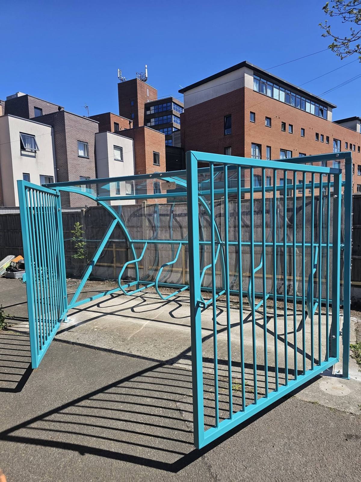 Teal cycle shelter with one security gate open showing the racks inside