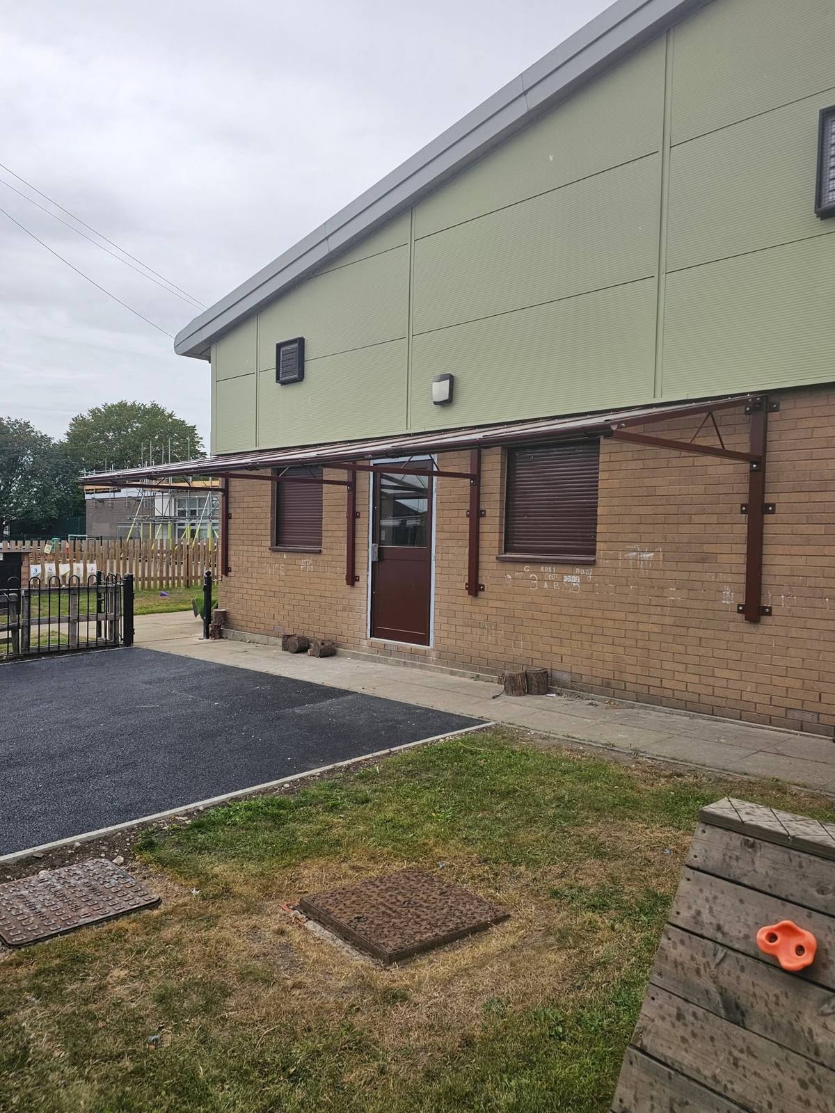 Brown cantilever canopy mounted along a brick wall above doorway and windows at Moss Valley Primary Academy, Manchester