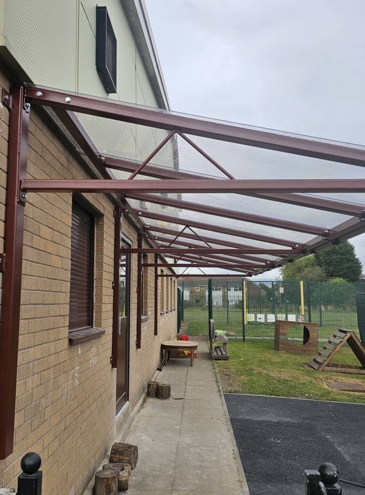 Underside view of the brown cantilever canopy showing the roof trusses along the brick wall