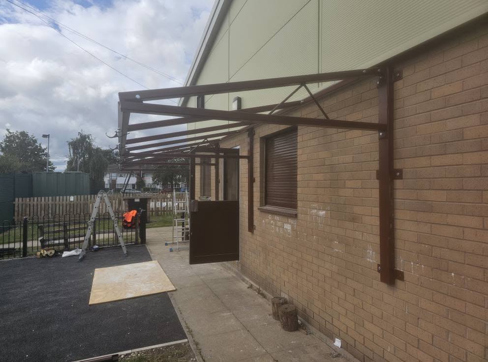 Angled view of the brown cantilever canopy frame against the brickwork with installation tools below