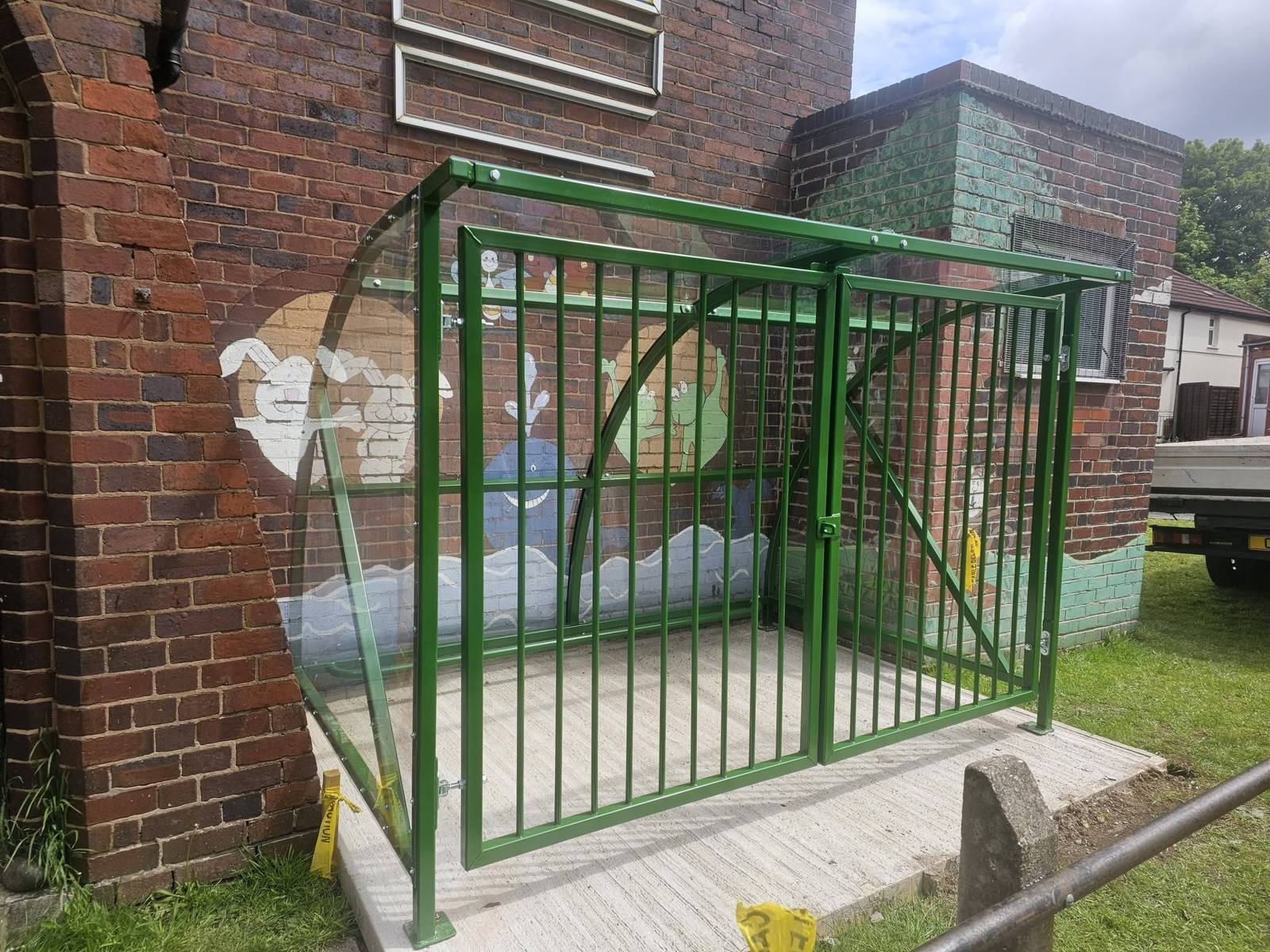Angled view of the green gated shelter beside an arched doorway and children's mural