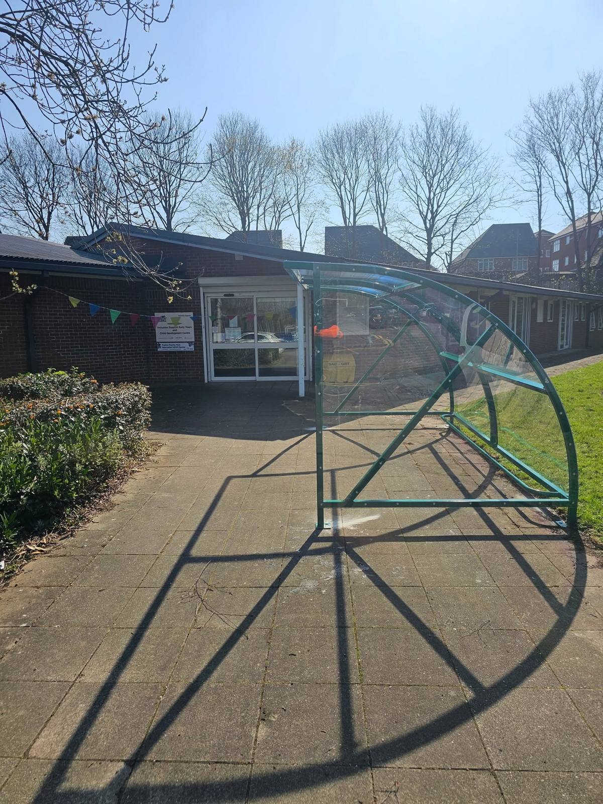 Side view of the green curved canopy casting its shadow across the paving by the entrance