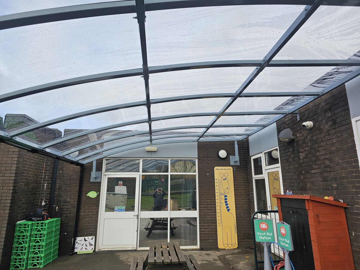 Underside of a curved canopy showing the powder-coated steel rafters and clear polycarbonate roof sheets