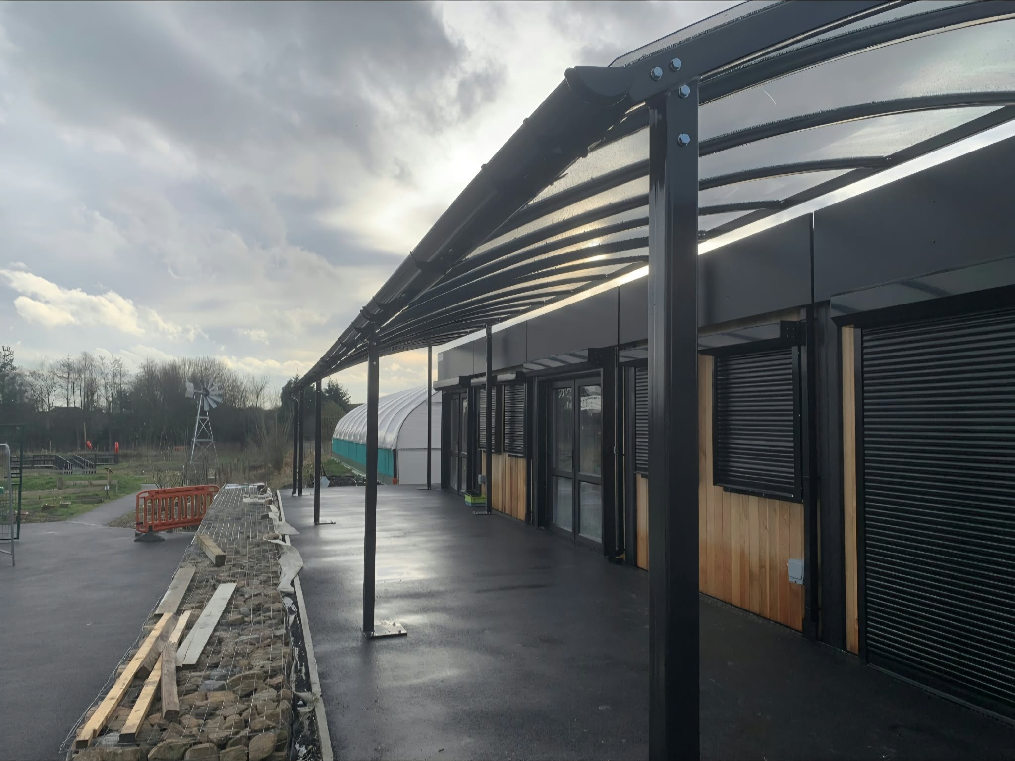 Dark anthracite curved canopy with a clear polycarbonate roof running along a school building in York