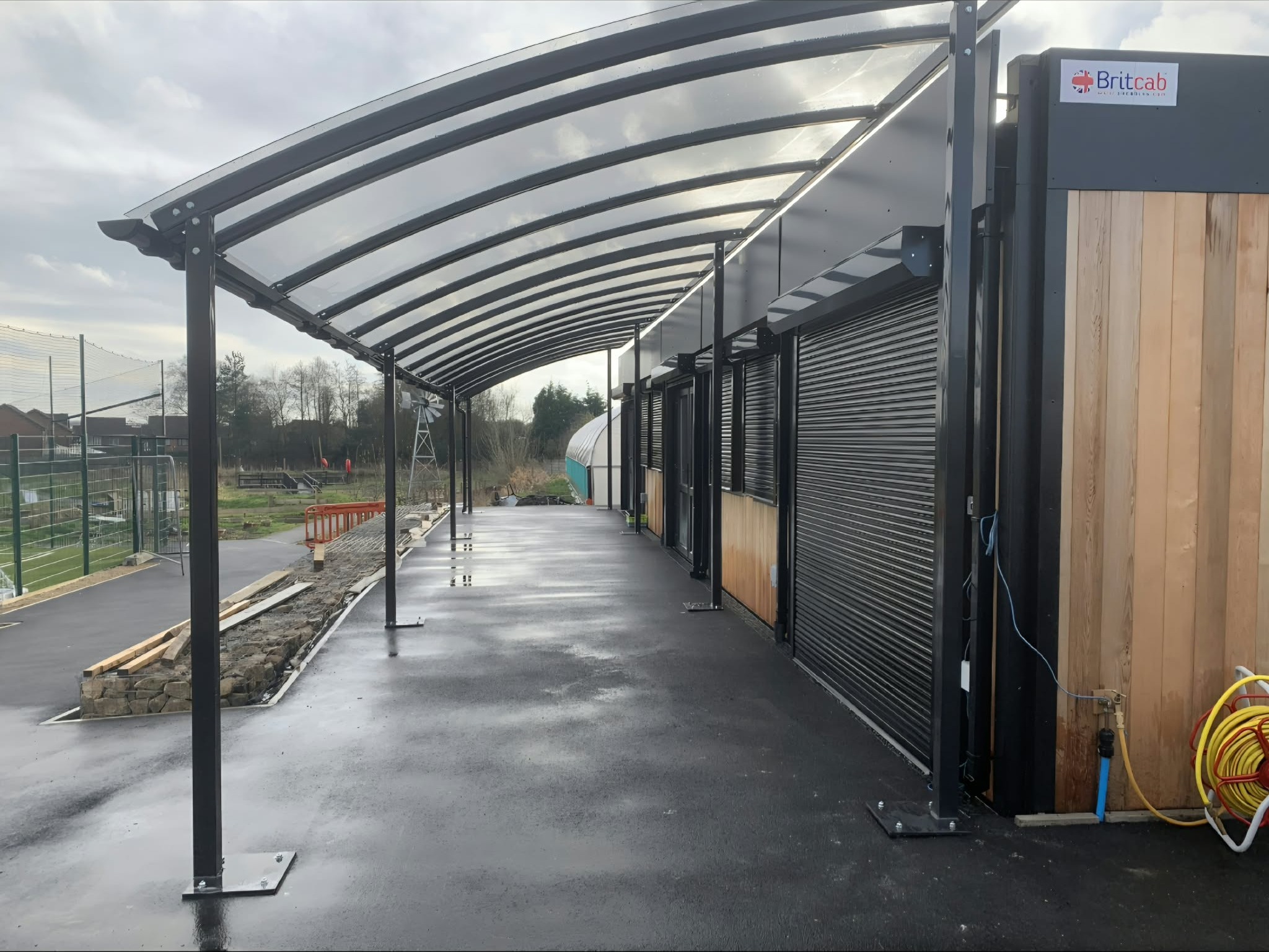 Looking along the covered walkway from the far end, the curved clear roof beside the building and growing area