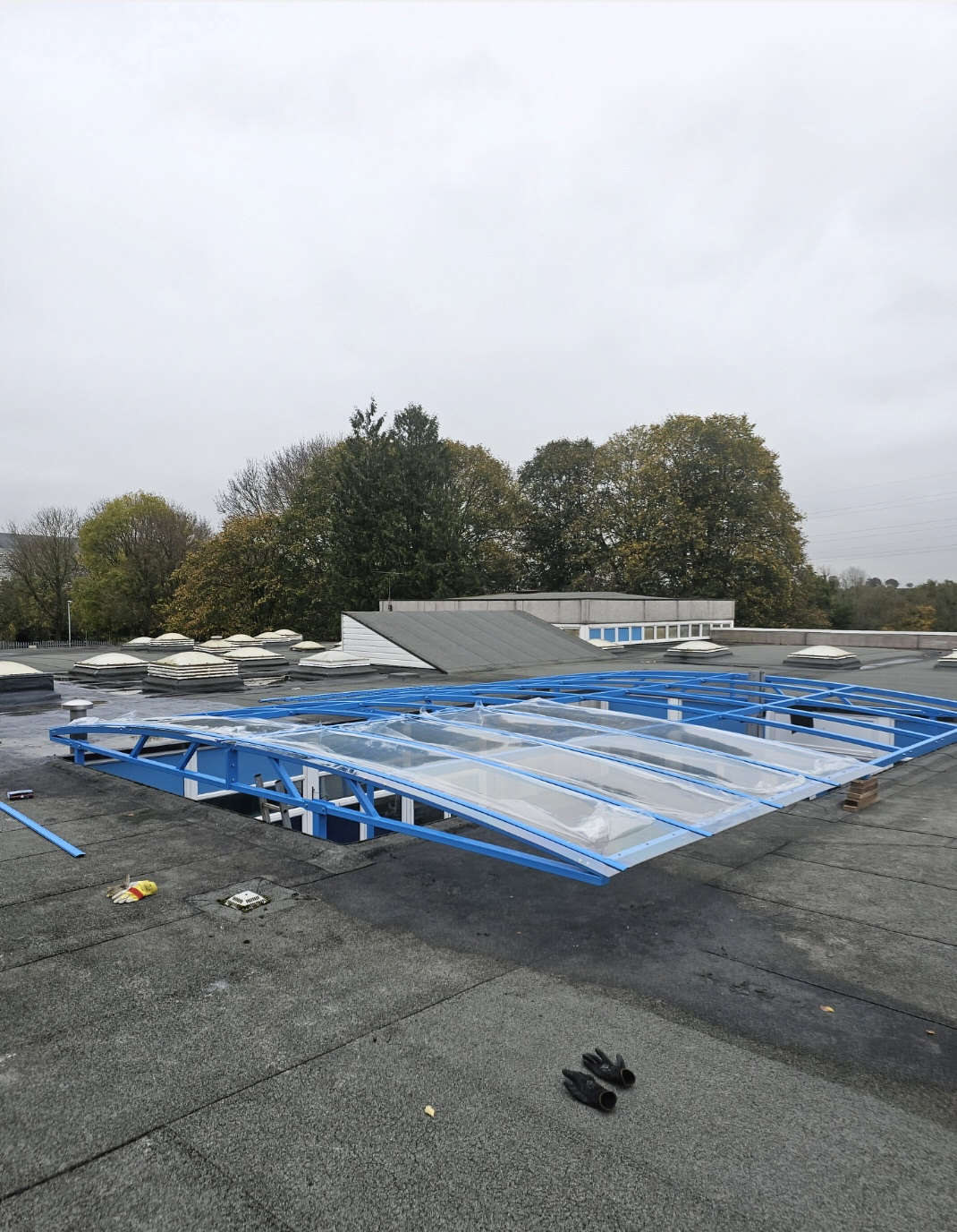 Close view from the flat roof of the blue curved canopy frame and clear panels spanning the courtyard
