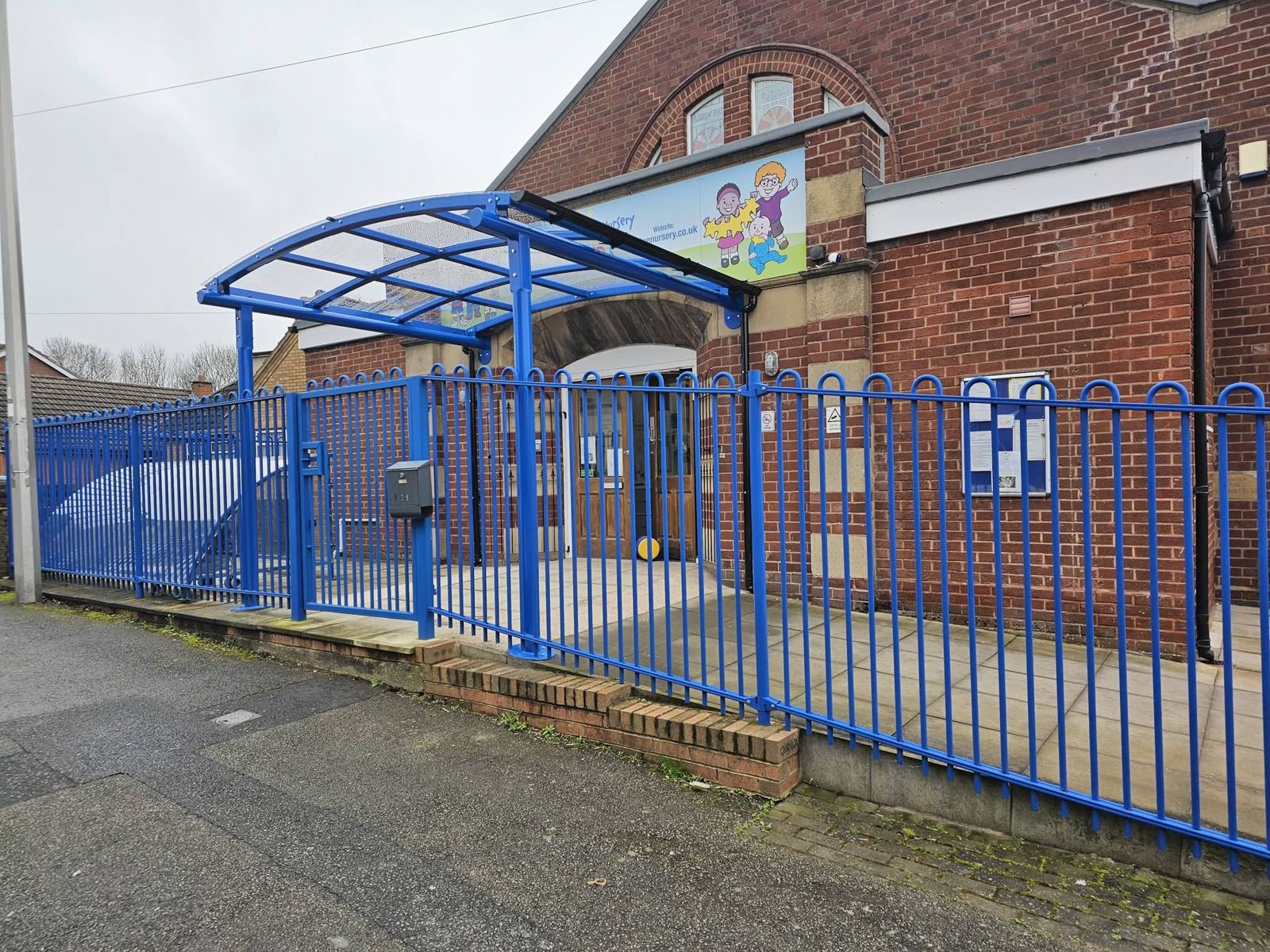 Blue curved entrance canopy behind railings at Shine Nursery's main gated entrance