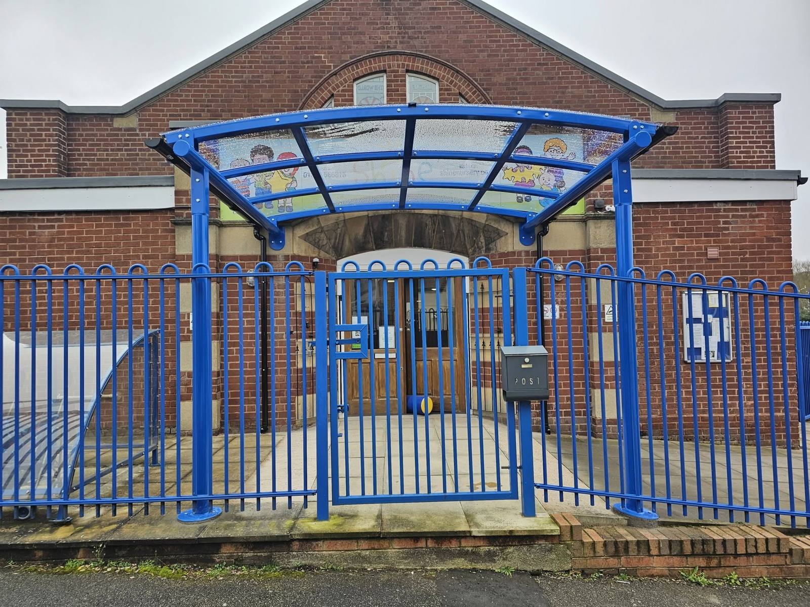 Front view of the arched blue entrance canopy above the gated doorway at Shine Nursery