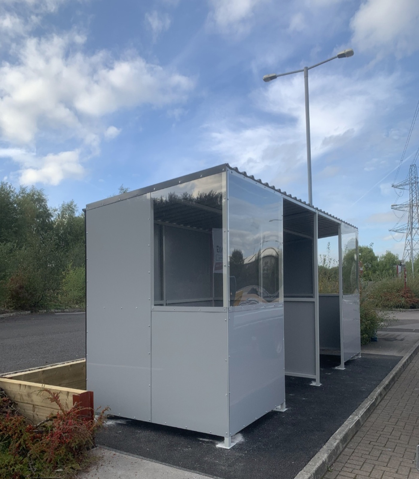 Side view of an enclosed glazed smoking shelter under a cloudy sky