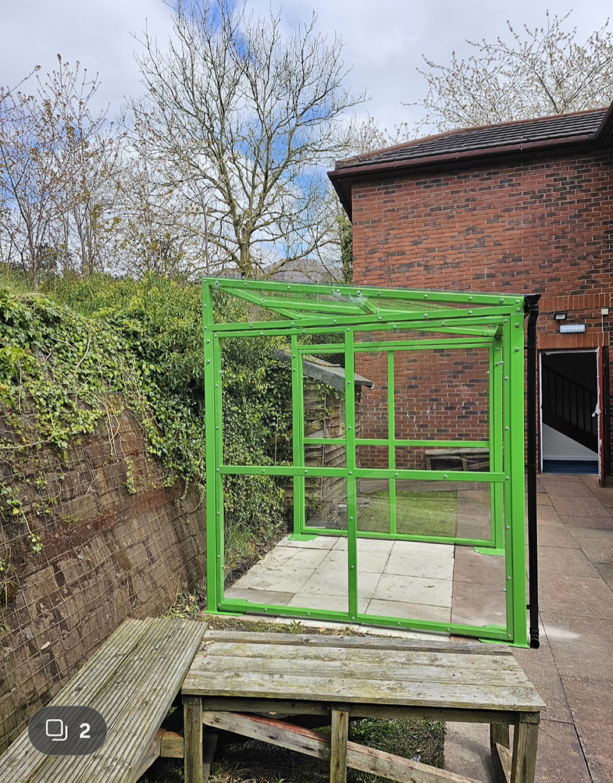 Front view of a green glazed shelter frame against a brick building