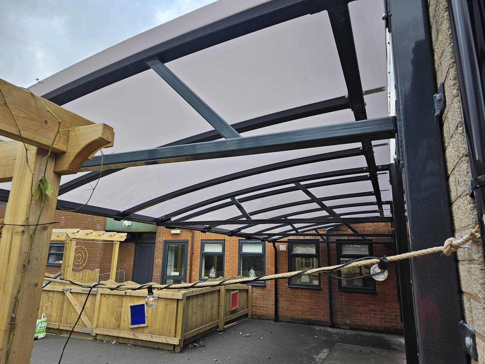 Looking up at the underside framework of the dark curved canopy spanning the playground