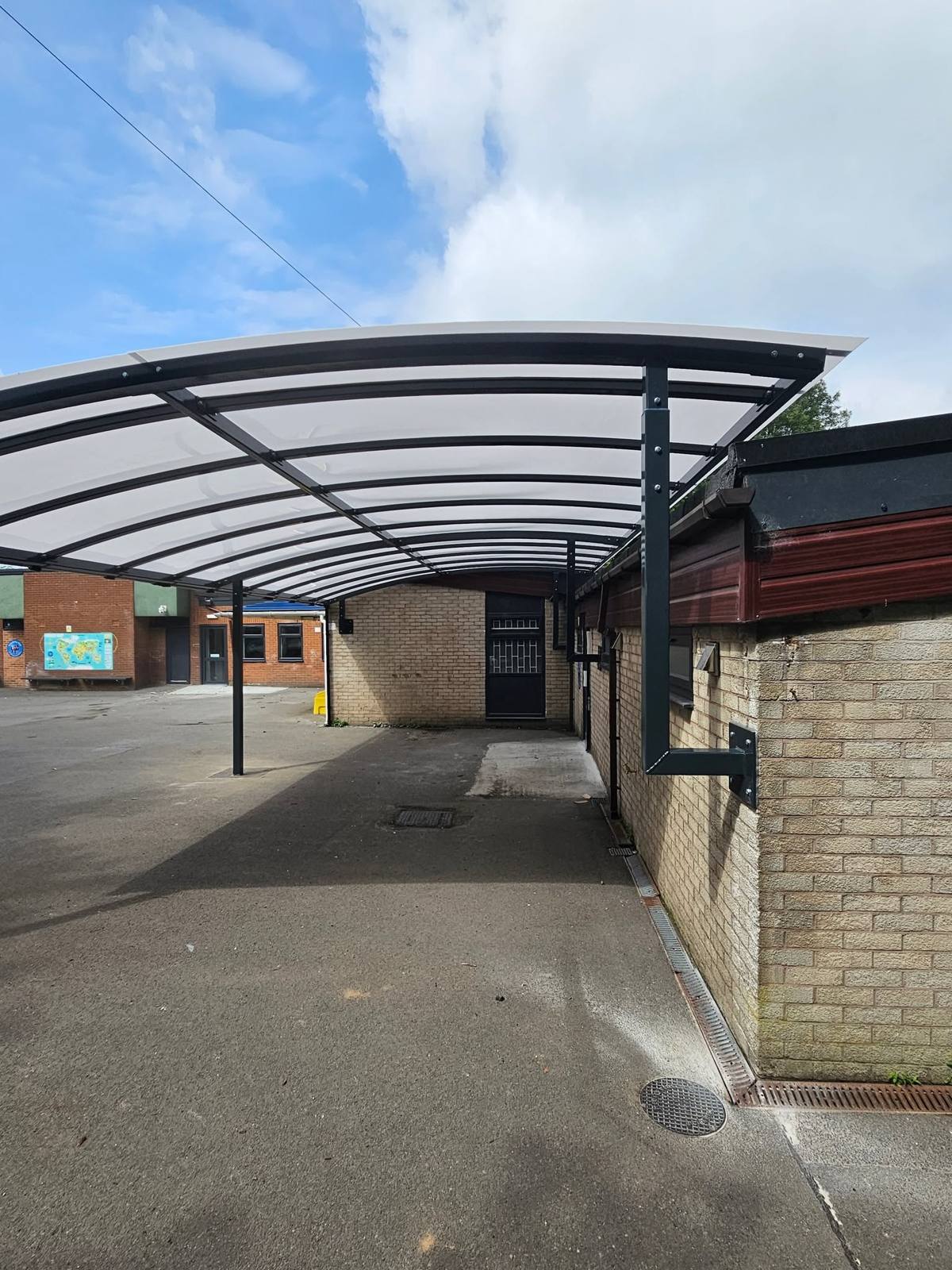 Curved monopitch canopy with dark steel frame covering a pathway beside the nursery at St Luke's Primary School, Oldham