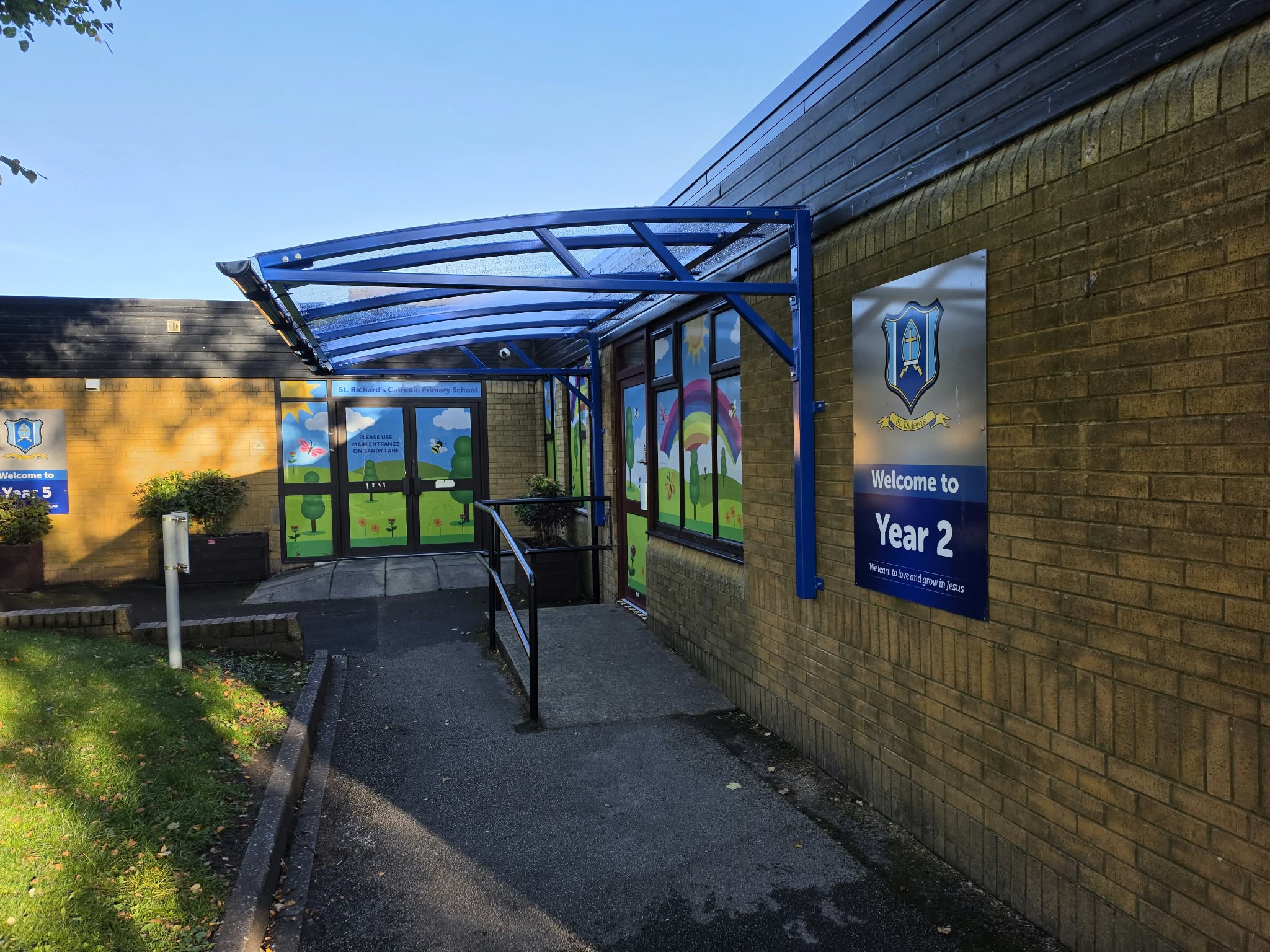 Angled view along the building of the blue cantilever waiting shelter above the Year 2 entrance ramp