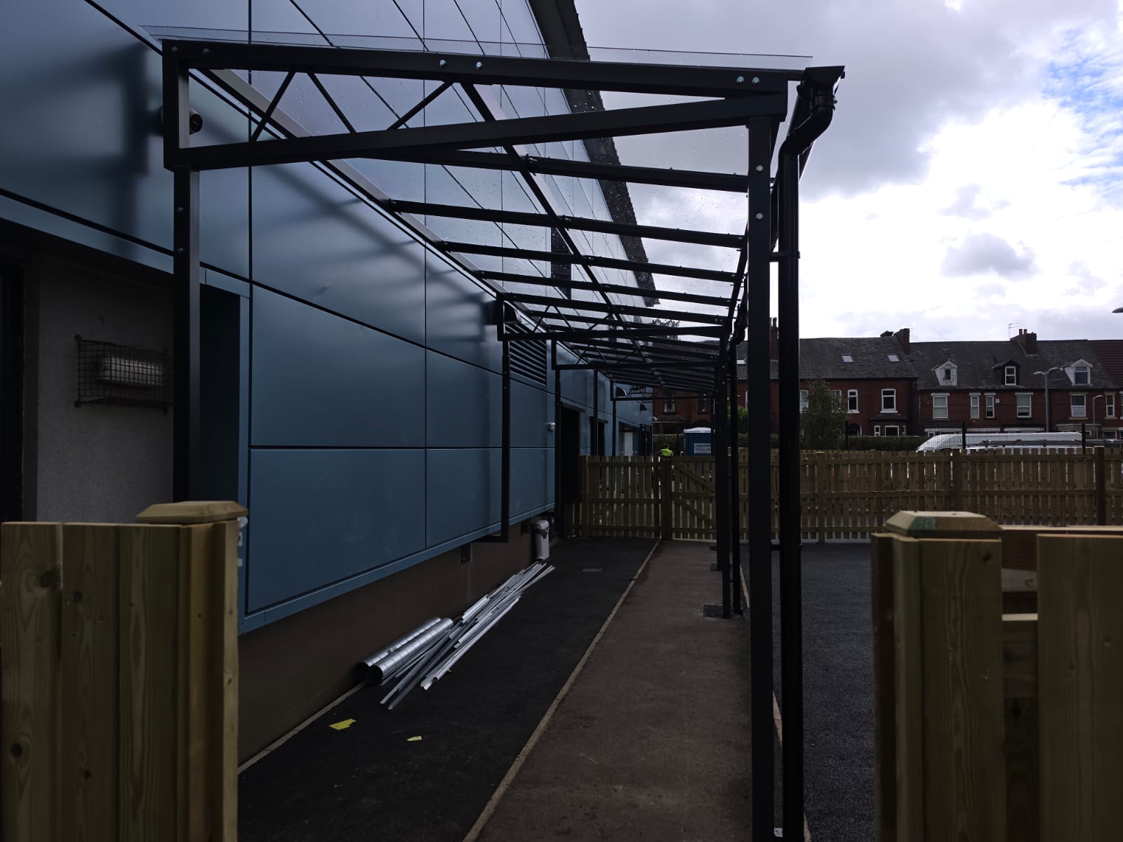End-on view along the covered walkway with its sloped glazed roof beside the blue cladding