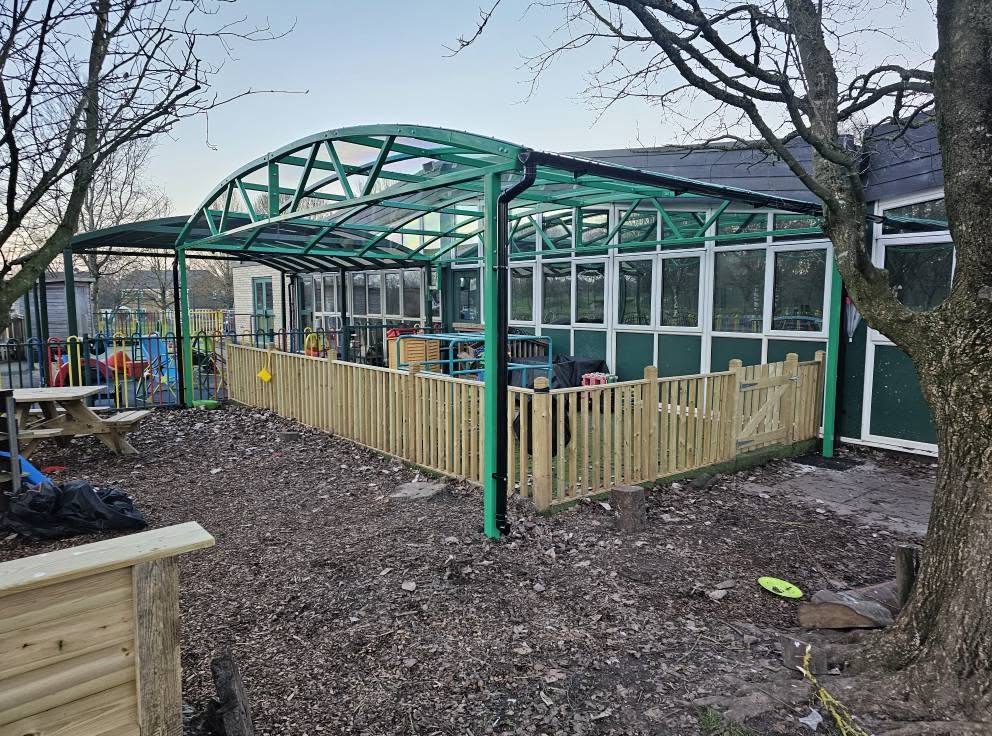 Curved play-area canopy over a fenced playground at Trinity Primary School