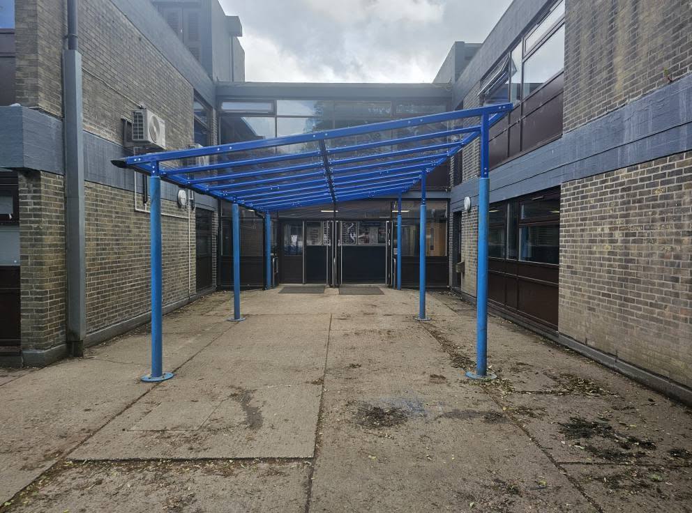 Blue steel entrance canopy over a courtyard walkway between buildings at Up Holland High School