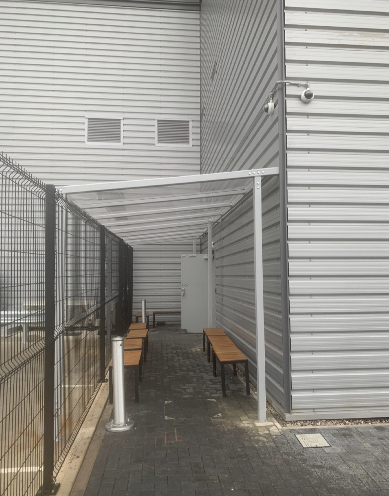 Angled view of a covered seating canopy with benches between two walls