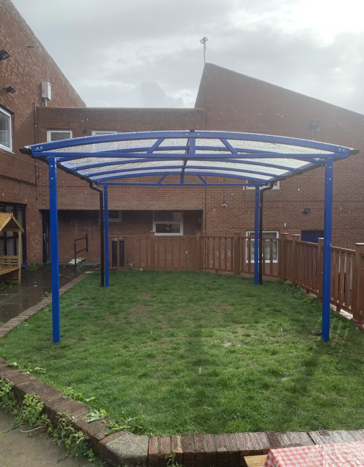 Blue curved-roof free-standing shelter on a grassed area in the rain