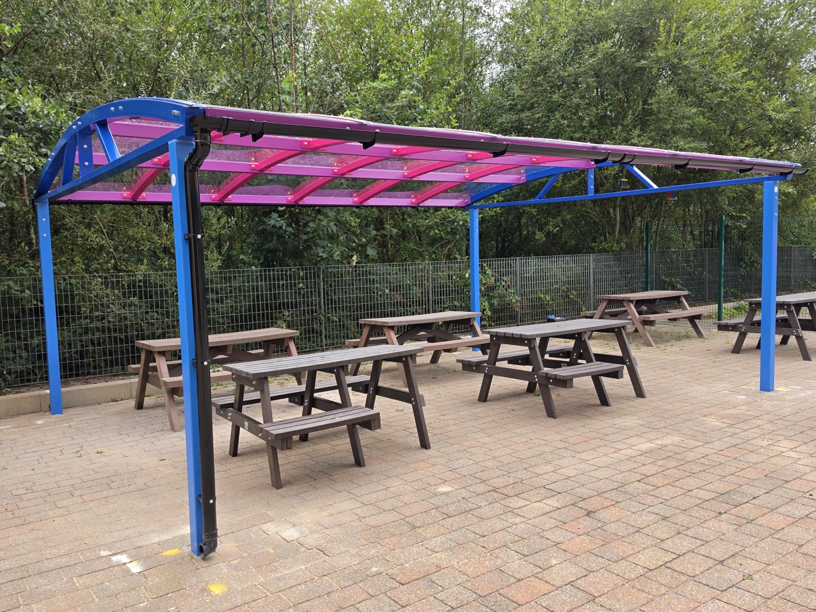 Angled view under the curved canopy roof showing pink support beams and bench seating