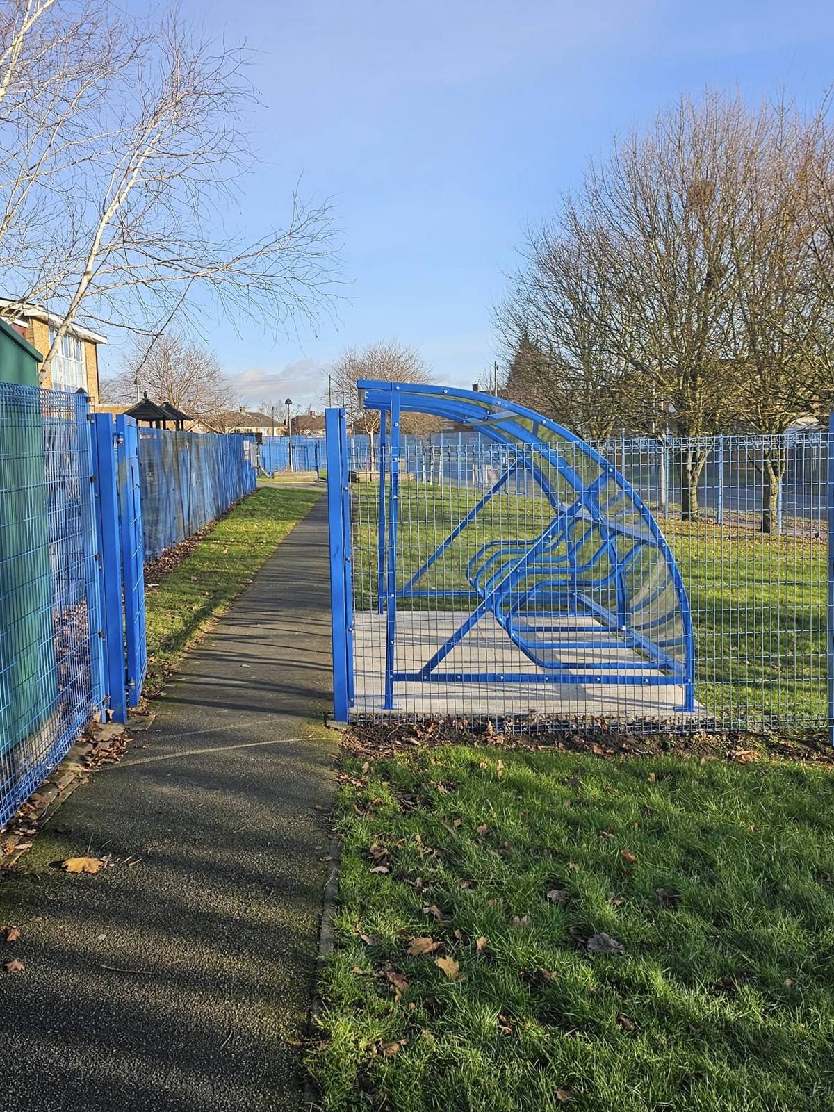 Blue cycle shelter end-on beside a footpath and mesh fencing under a clear winter sky at Woodside Academy, Bradford